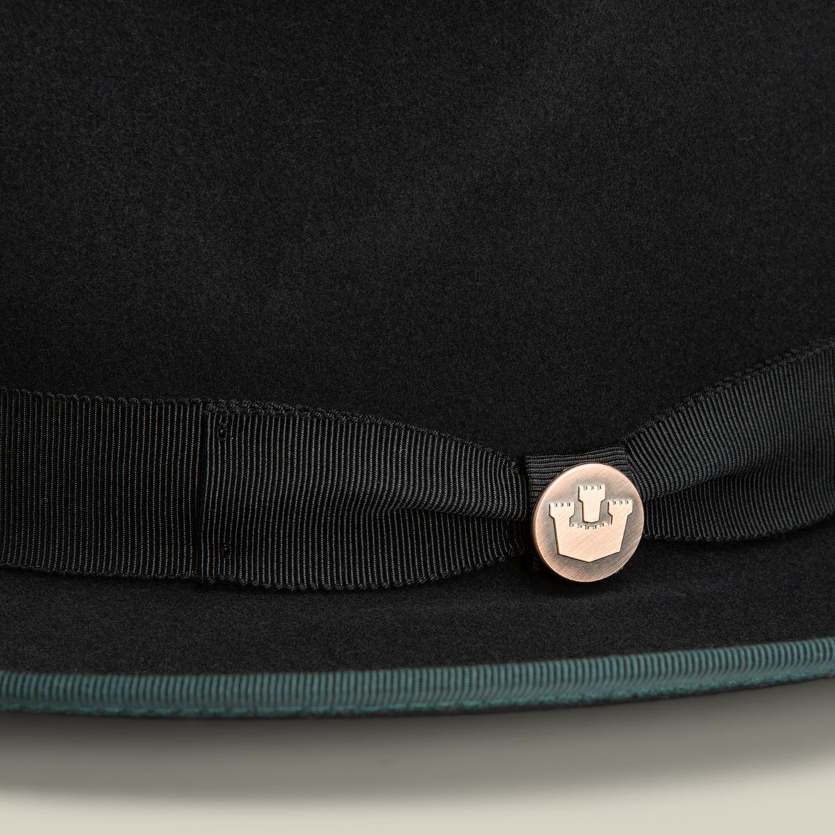 Close-up of the Goorin Bros. “River Gray,” an American-made black merino wool fedora, featuring a ribbon band and a round metallic emblem with a castle design.