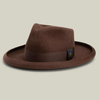 The Colonel Pierce by Goorin Bros. is a brown felt fedora with a teardrop crown, wide brim, dark brown band, and a small round metallic accent on the side, shown on a neutral background.
