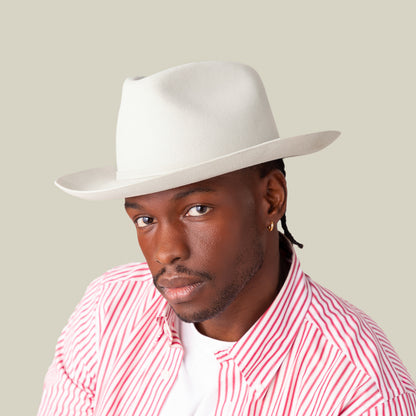 A man wearing the Goorin Bros. Night Hawk, an all-season fedora with a wide snap brim and teardrop crown, pairs it with a red and white striped shirt and white tee, posing against a plain beige background.