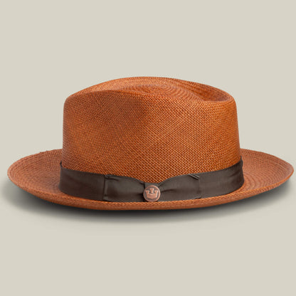 The Goorin Bros. John Sr. is a brown toquilla teardrop fedora with a medium brim, 50 UPF sun protection, a dark brown ribbon band, and a round metallic pin on the side, shown against a plain light background.