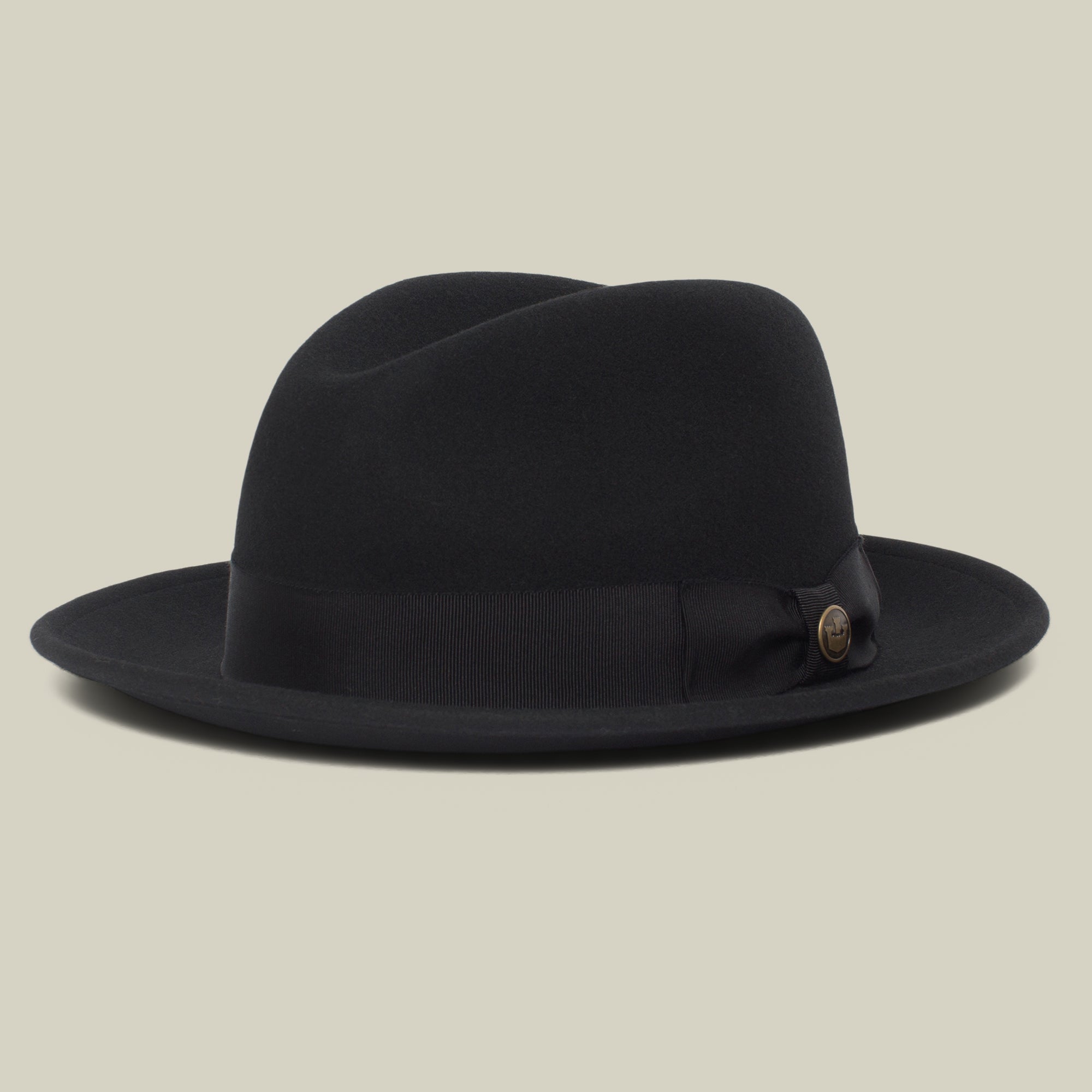 Dean the Butcher by Goorin Bros. is a black American-made fedora with a wide brim, grosgrain hatband, and small round button detail, shown on a light beige background.