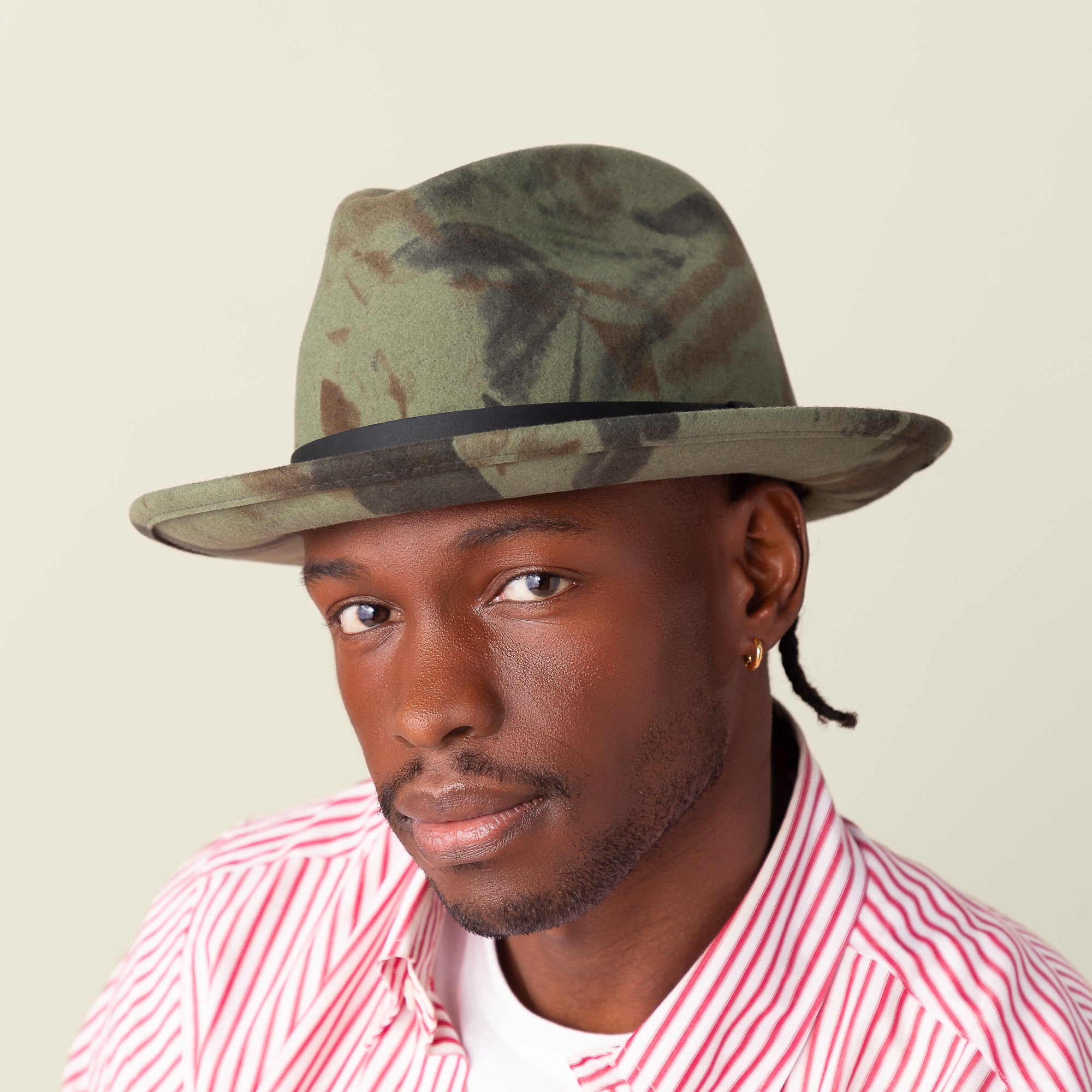 A man wears Goorin Bros.' Dean the Butcher all-season hat with a wicking sweatband, paired with a gold hoop earring and a red and white striped shirt, looking at the camera against a plain background.