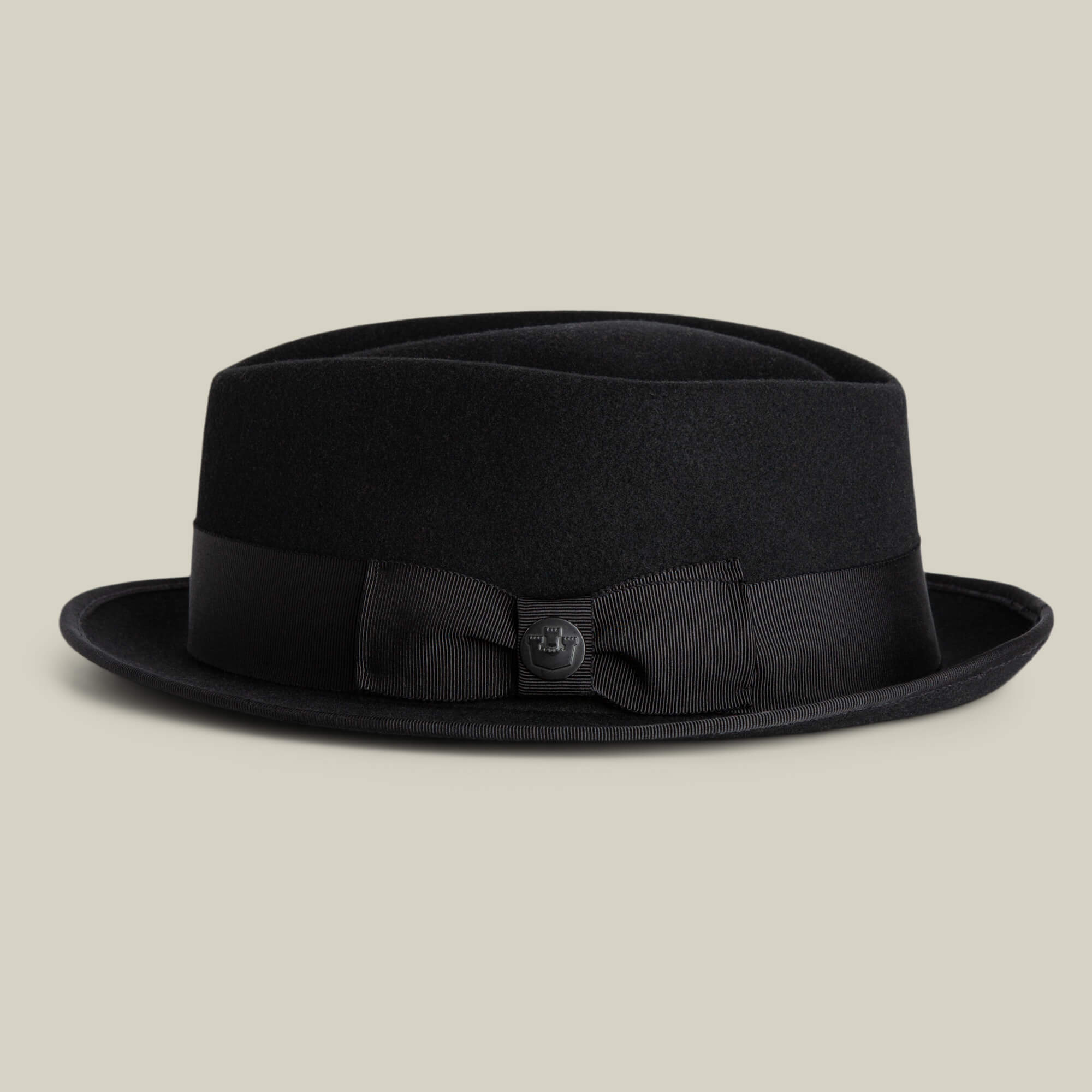 The Goorin Bros. Slick Carter is a black wool pork pie hat with a flat crown, short brim, and black ribbon band detailed with a bow and button—ideal for adding stylish flair to any look.