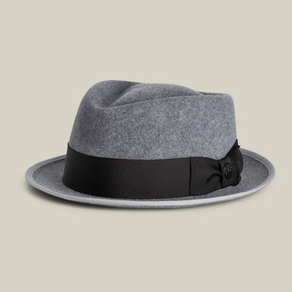 The Slick Carter by Goorin Bros. is a grey felt fedora featuring a black grosgrain ribbon band and bow, plus a wool short brim. Displayed on a neutral background, it brings effortless style and timeless elegance to any look.