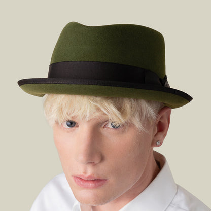 Effortlessly stylish, a platinum blonde person wears the Goorin Bros. Slick Carter green wool short brim fedora with a black band, paired with a white collared shirt and diamond stud earring, facing the camera against a plain background.