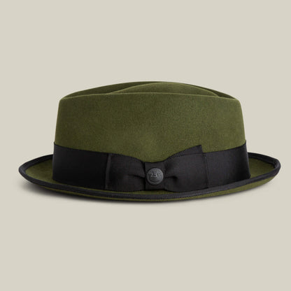 The Goorin Bros. Slick Carter is an olive green wool short brim fedora with a black ribbon band and small decorative button, shown against a plain beige background, reflecting effortless style.