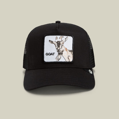 The Goorin Bros. Goat Beard is a black trucker hat with a mesh back panel and a white patch featuring an illustrated goat and text reading "GOAT" on the front, shown against a neutral beige background.