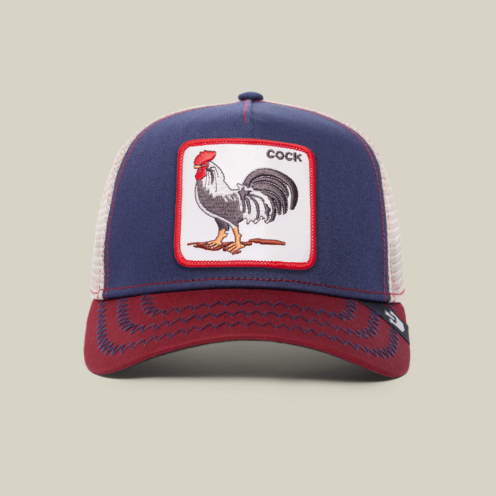 The Farm's "The Cock" cap features blue and red panels, a white mesh back, and a rooster patch with the word COCK on the front—a standout piece for bold, playful style.