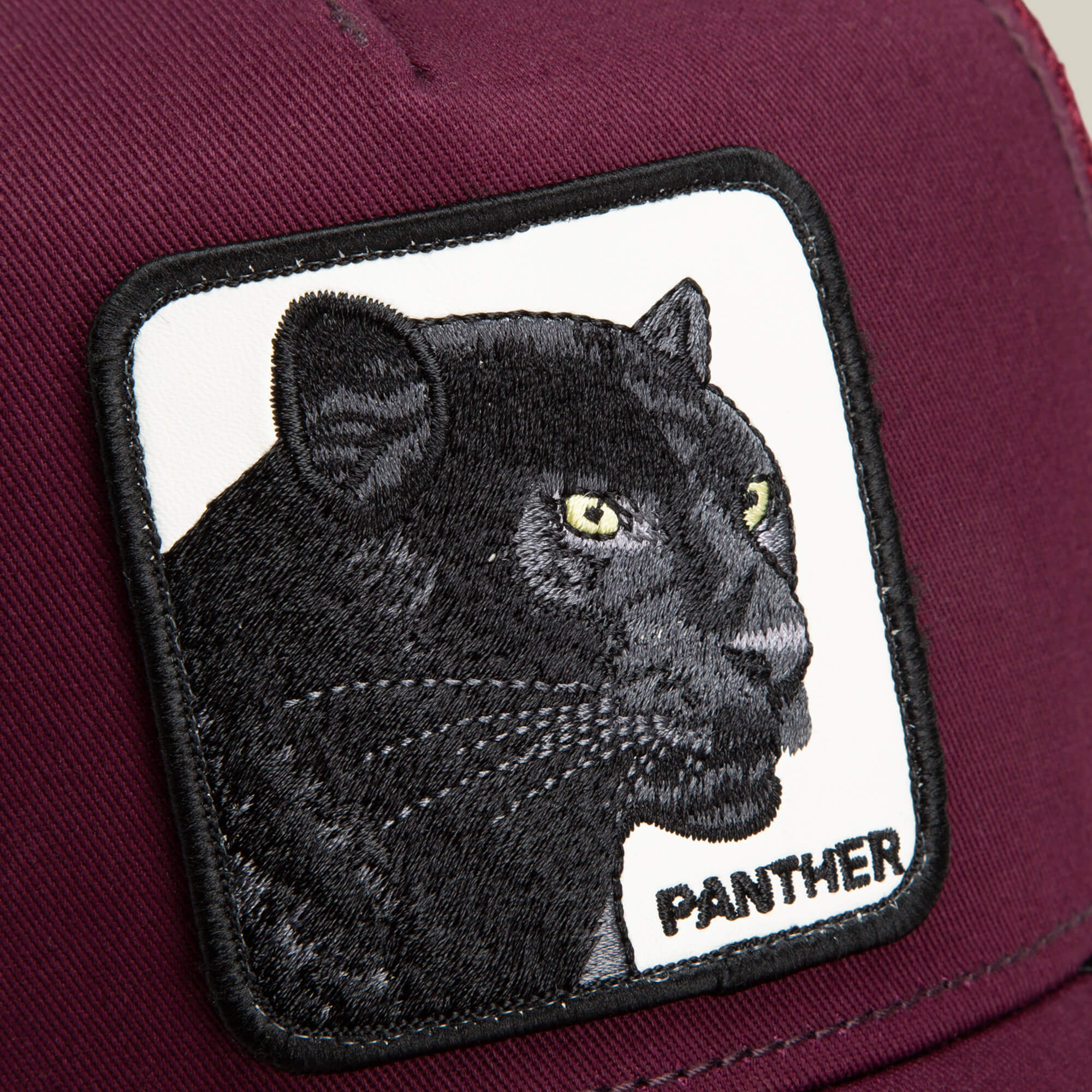 A close-up of The Panther trucker hat by Goorin Bros., showing a maroon cap with a patch featuring an embroidered black panther and “PANTHER” in black letters.