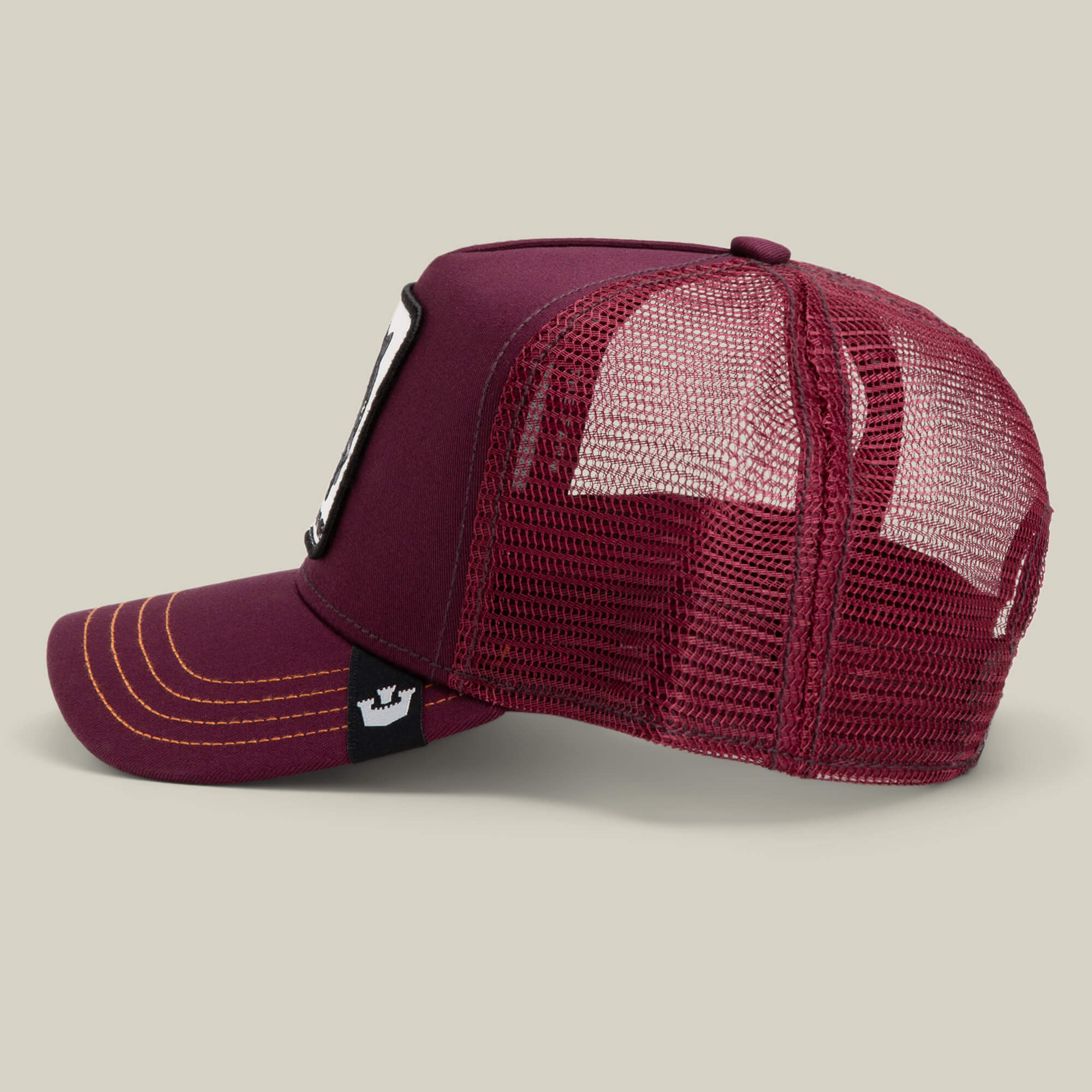 The Panther by Goorin Bros. is a maroon trucker baseball hat with yellow stitching, mesh back panels, and a white rectangular patch on the front—displayed on a neutral background for a stylish nod to The Farm.