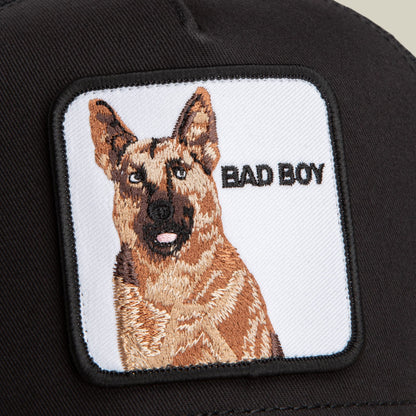 The Bad Boy by Goorin Bros is a black trucker cap featuring an embroidered German Shepherd patch with "Bad Boy" text on a white background.