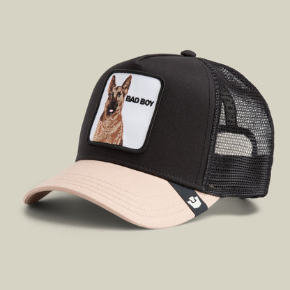 The Bad Boy by Goorin Bros is a black and beige mesh trucker hat featuring an embroidered dog patch with "BAD BOY" text on the front panel, shown in a studio product shot.