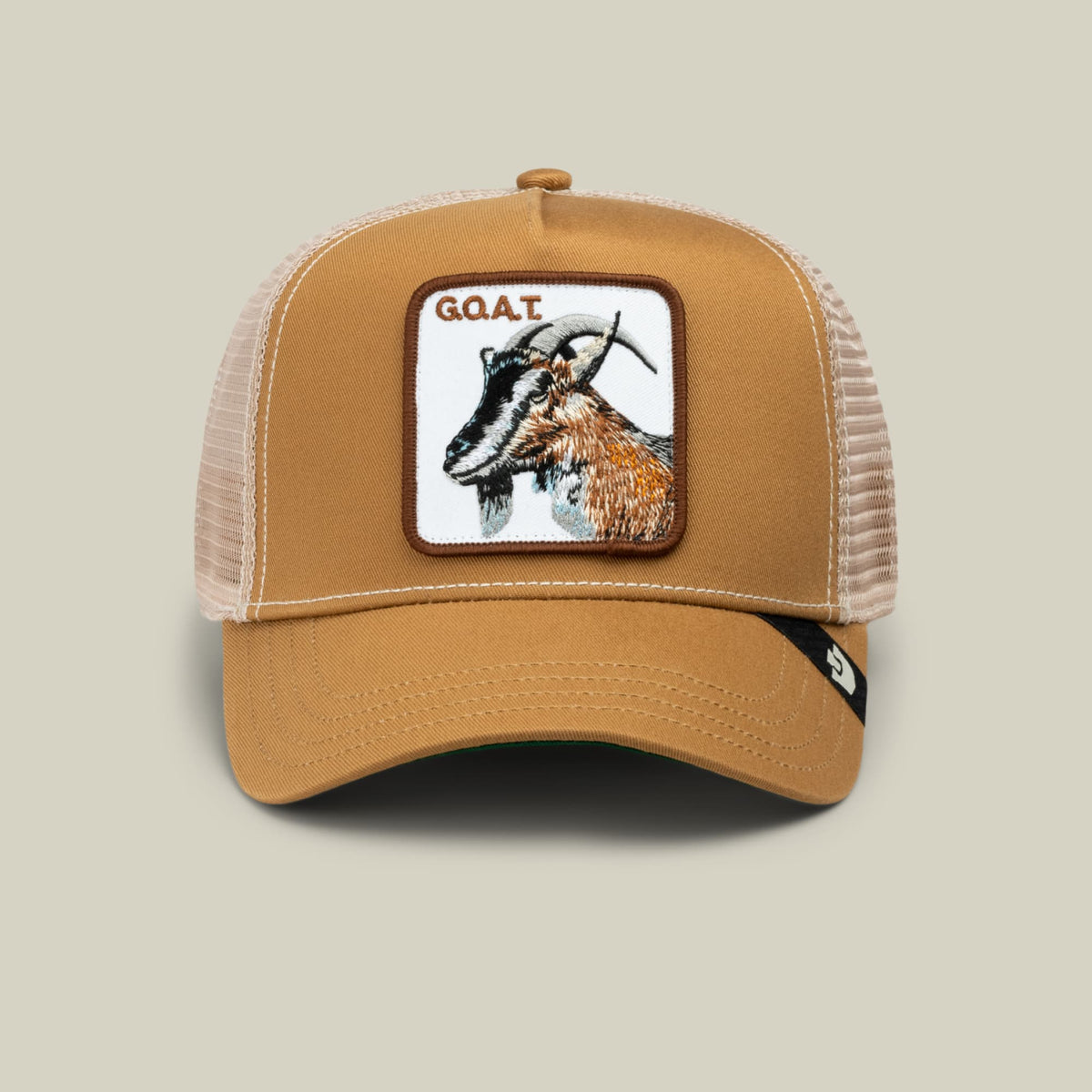 The GOAT by Goorin Bros is a tan and cream mesh trucker hat featuring an embroidered goat patch on the front, displayed against a neutral background.