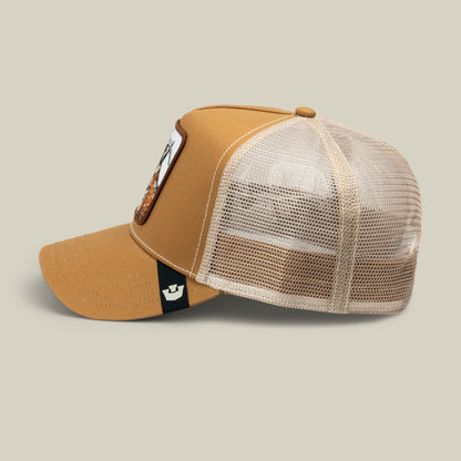 The GOAT by Goorin Bros is a tan and cream mesh trucker hat with a structured front panel, decorative side patch, and black chin strap detail, displayed against a neutral background.