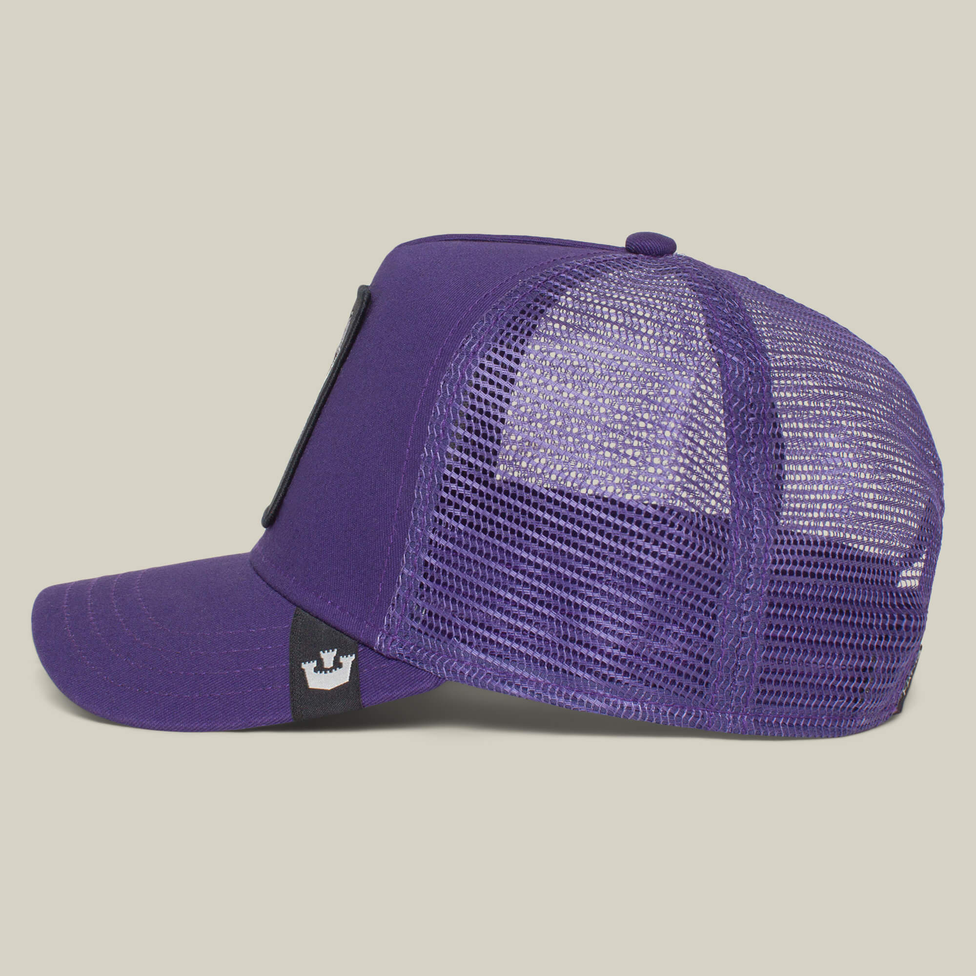 The Farm’s “The Lone Wolf” trucker cap is shown in purple mesh from the side, with a curved brim and a black tag featuring a white crown logo near the adjustable back—a bold pick for independent spirits.