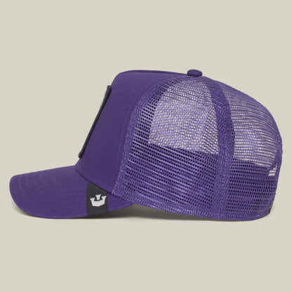 The Farm’s “The Lone Wolf” trucker cap is shown in purple mesh from the side, with a curved brim and a black tag featuring a white crown logo near the adjustable back—a bold pick for independent spirits.