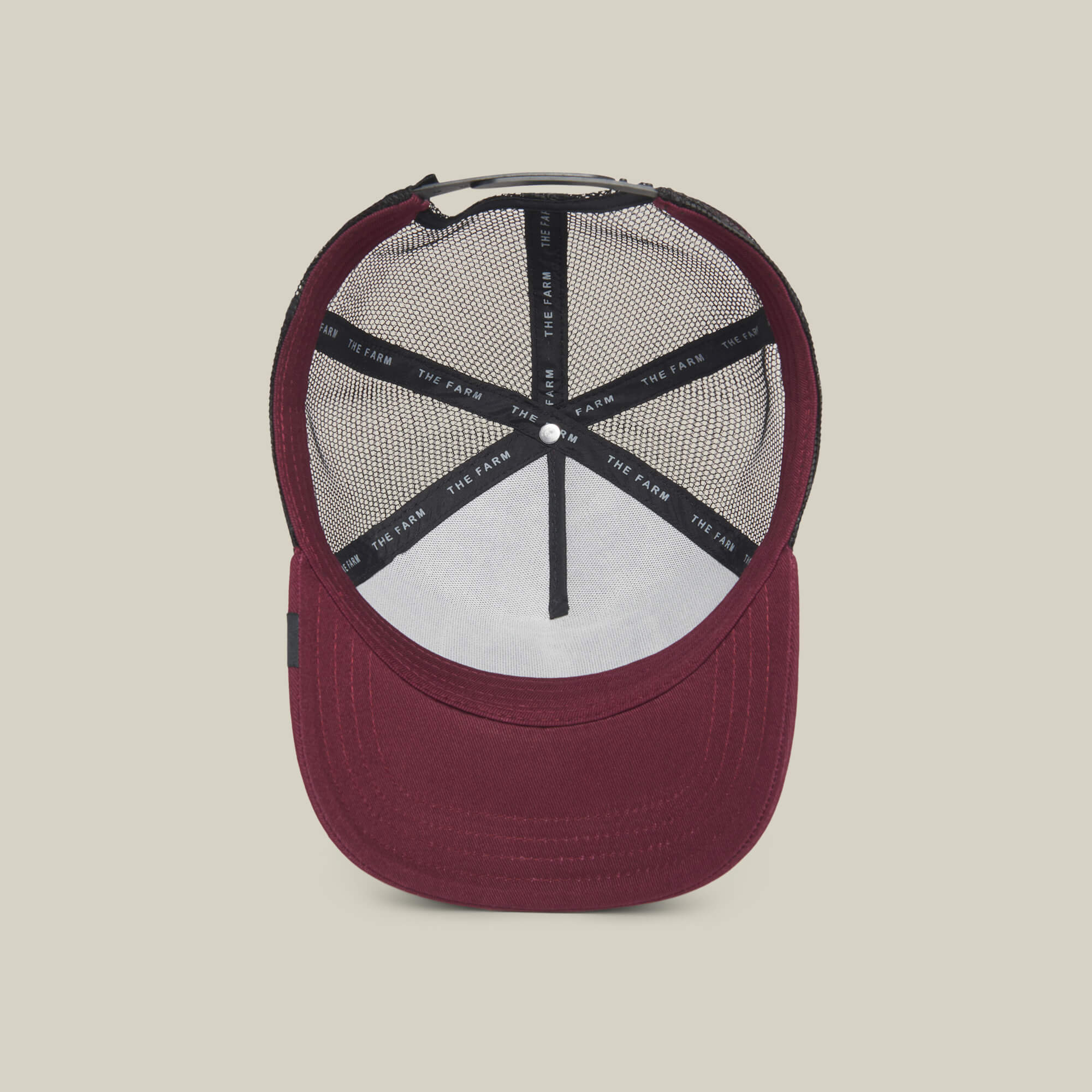 The Lone Wolf by The Farm: a burgundy trucker hat seen from above, revealing black mesh lining and inner label on a light beige background—ideal for independent spirits and anti-conformists.