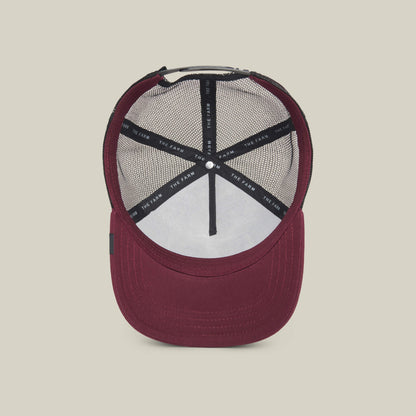 The Lone Wolf by The Farm: a burgundy trucker hat seen from above, revealing black mesh lining and inner label on a light beige background—ideal for independent spirits and anti-conformists.