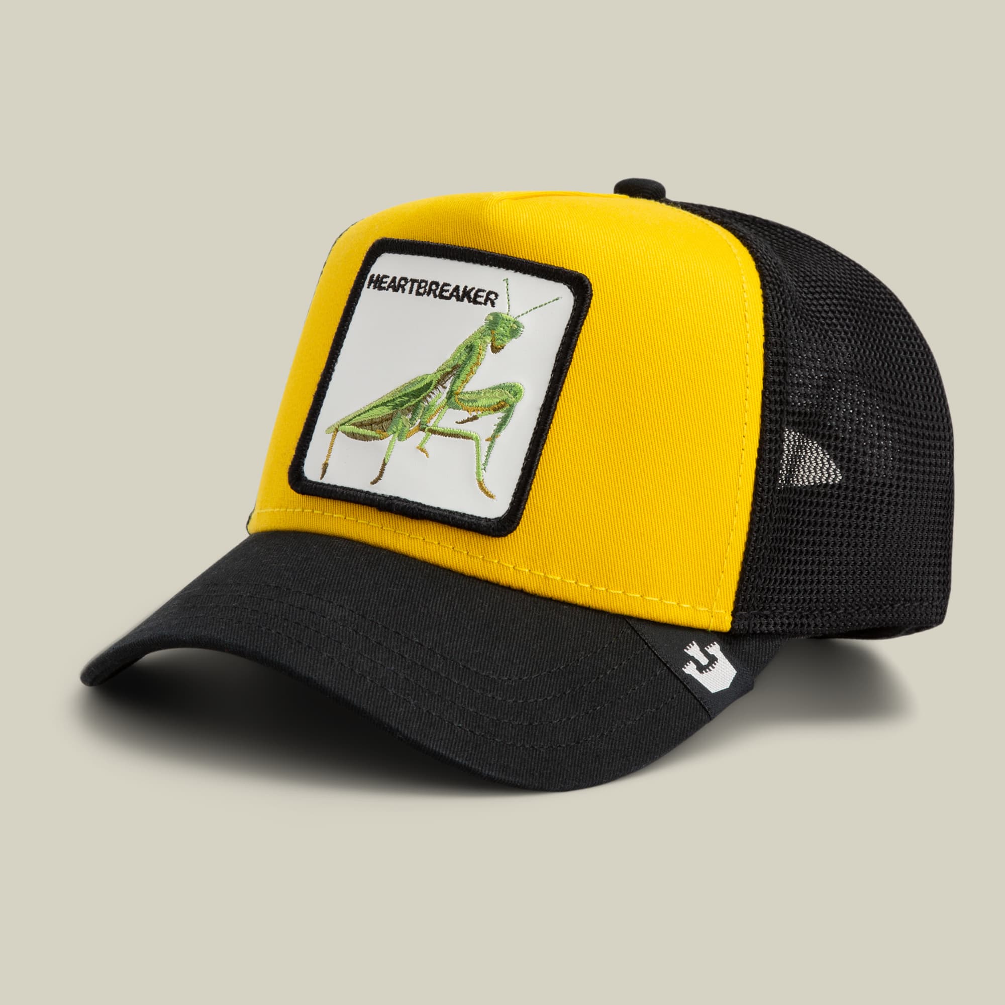 The Heartbreaker by Goorin Bros is a yellow and black mesh trucker hat featuring a green mantis patch with "Heartbreaker" text on the front panel, displayed against a neutral background.