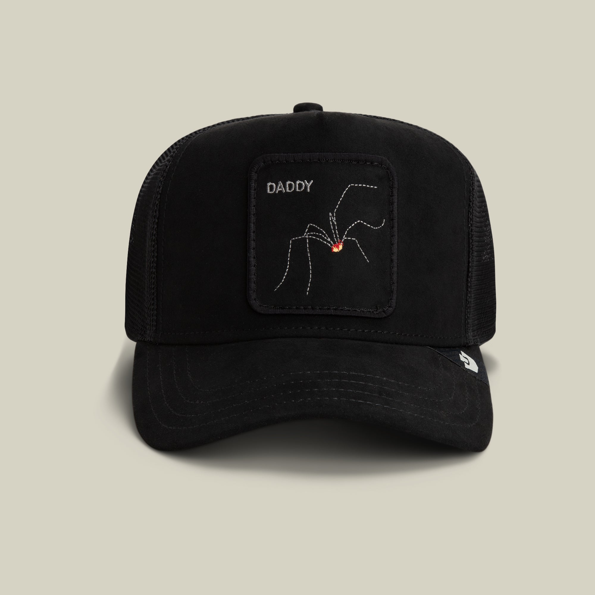 Introducing The Suede Spider by Goorin Bros.—a void black microsuede trucker hat showcasing a bold “DADDY” embroidery above a distinctive patch featuring a red-marked spider. This classic cap fuses subtle dad-joke flair with standout style against its sleek, dark backdrop.