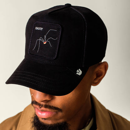A man wearing The Suede Spider hat by Goorin Bros.—a black microsuede cap featuring a spider arachnid and the word “DADDY” embroidered on the front patch—looks downward.