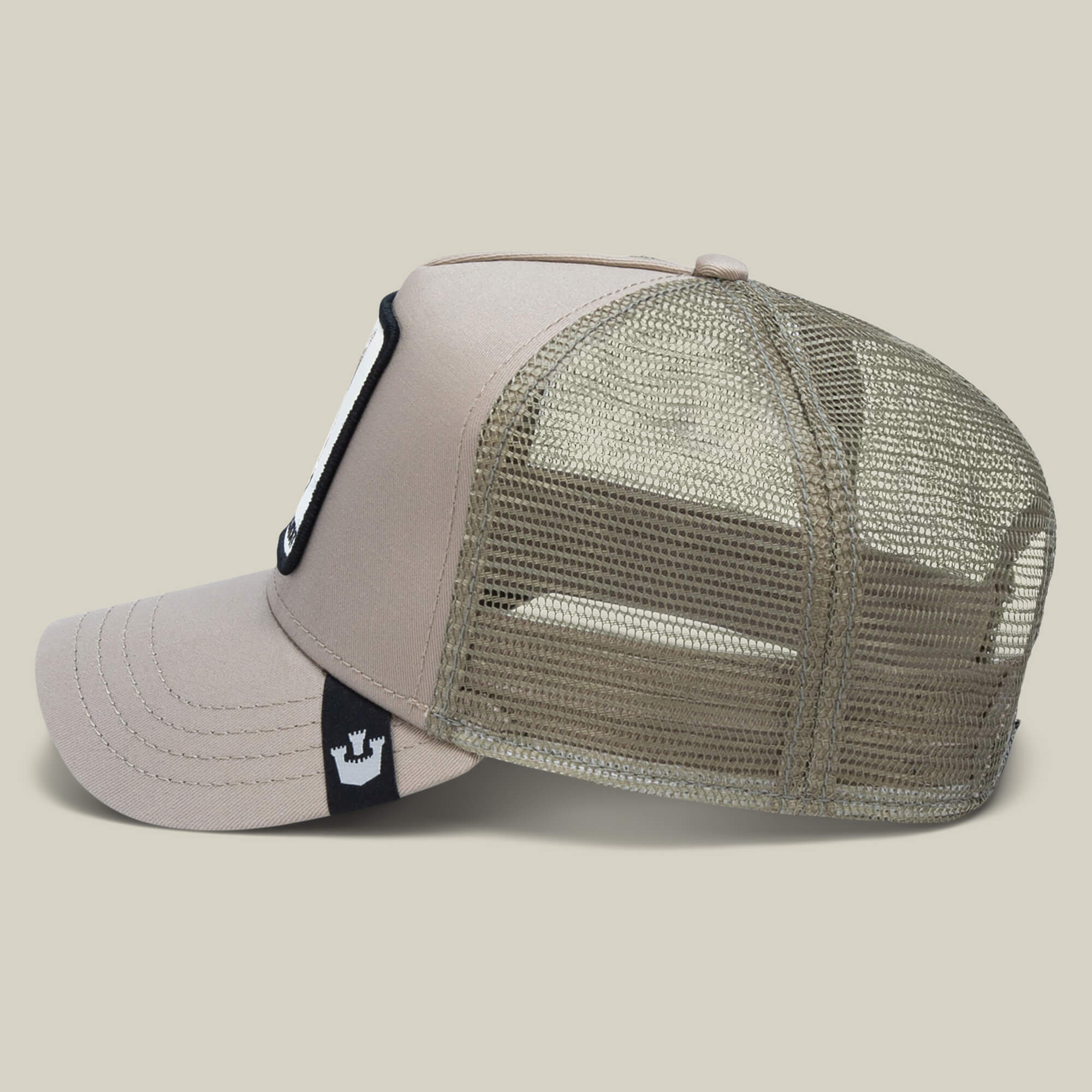 The Farm's "The Bandit Coyote" trucker hat features a beige and olive green design, mesh back, curved bill, and a black tag with white crown logo—ideal for adventurous spirits.