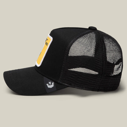 The EK65 Penguin by Goorin Bros. is a black mesh trucker cap with a curved bill, a rectangular yellow patch on the front, and a small crown logo tag on the side, displayed against a neutral background.