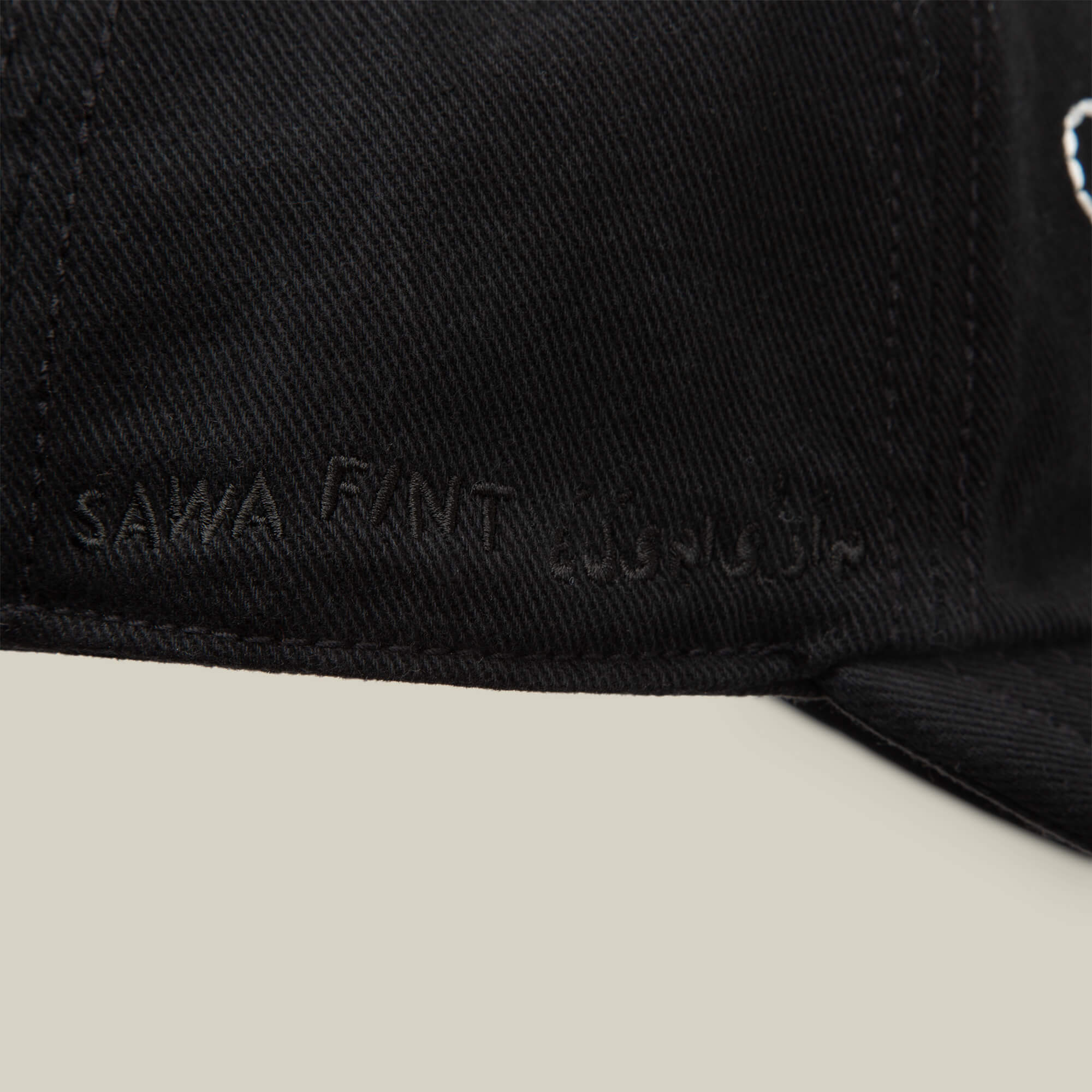 Close-up of a black papa cap from Goorin Bros.' Fine Headwear collection, featuring "Sawa Tant" and Arabic text embroidered in black thread on the side—showcasing stylish design.