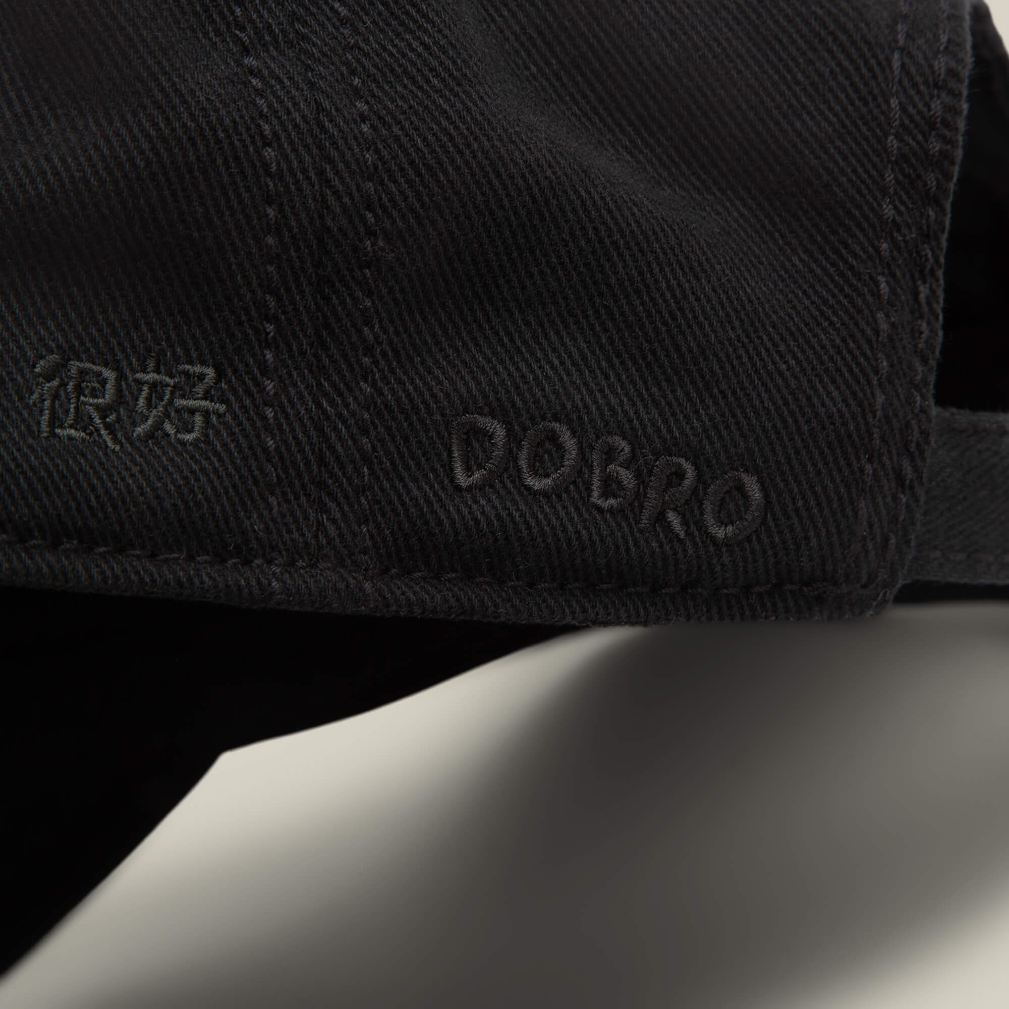 Close-up of a black Fine Headwear papa cap by Goorin Bros., featuring the word DOBRO and Chinese characters embroidered in matching black thread.
