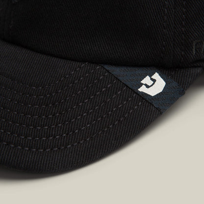 Close-up of the brim on Goorin Bros. Fine Headwear papa cap, featuring visible stitching and a small black tag with a white stylized letter G, showcasing premium quality.