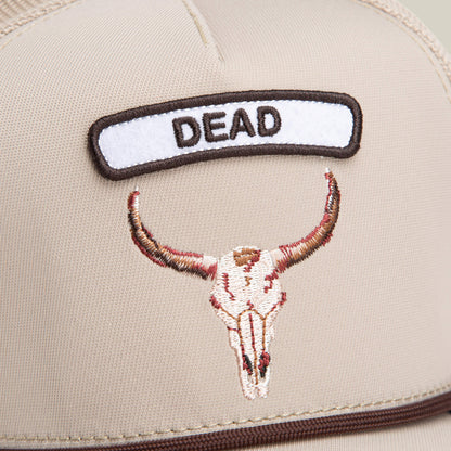 The GB2 Skull by Goorin Bros. is a beige trucker hat with desert tones, featuring an embroidered cattle skull patch and a bold "DEAD" patch above it.