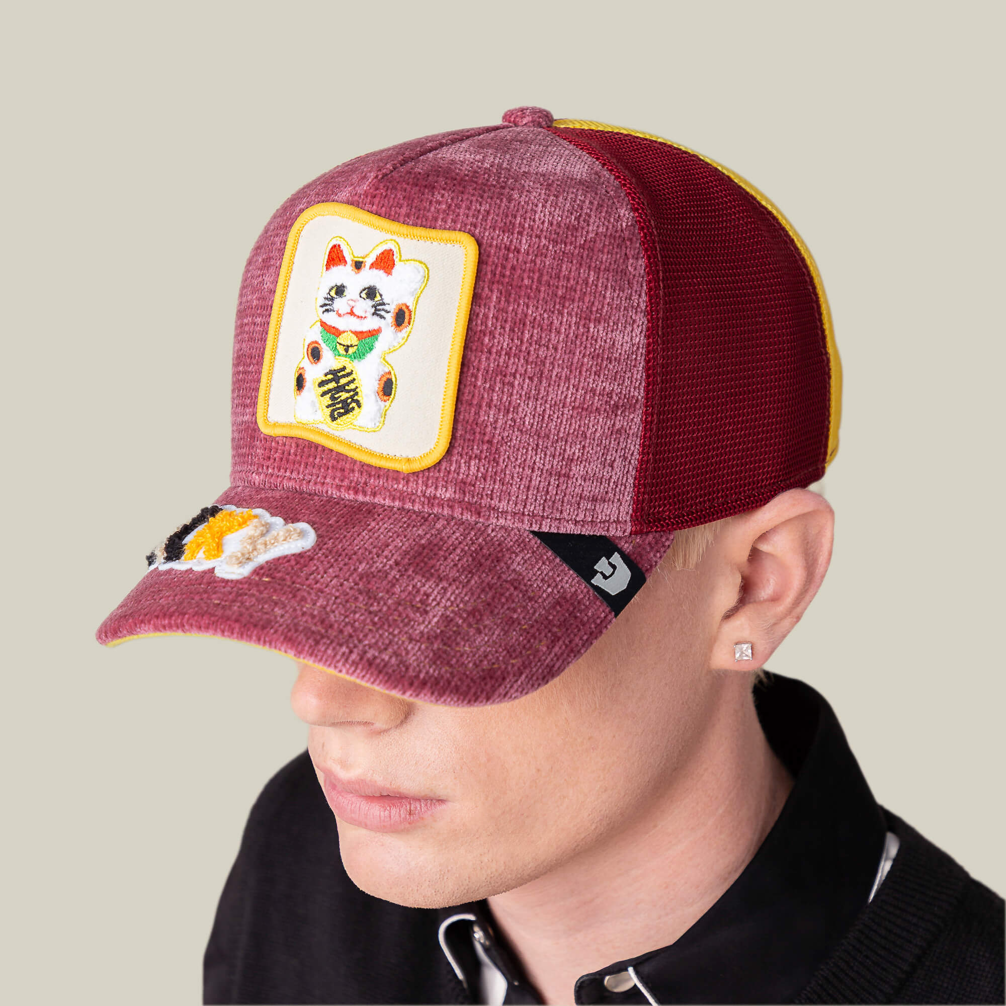 A person wears the Goorin Bros. Maneki-Neko maroon and yellow mesh cap, featuring a lucky cat patch on the front and a small embroidered cat on the visor, reminiscent of a playful LUCKY beanie, facing slightly downward.