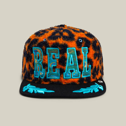 The El Camino cap by Goorin Bros. features fuzzy orange leopard sherpa, bold blue REAL lettering on the front, and aqua embroidery accents on a black brim for an eye-catching look.