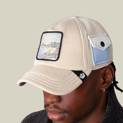 A person wears the Goorin Bros. AllmiMator beige cap with a landscape patch labeled OLD SCHOOL on the front, a small blue and white pocket patch on the side, paired with an old school sweater for a classic, timeless style.