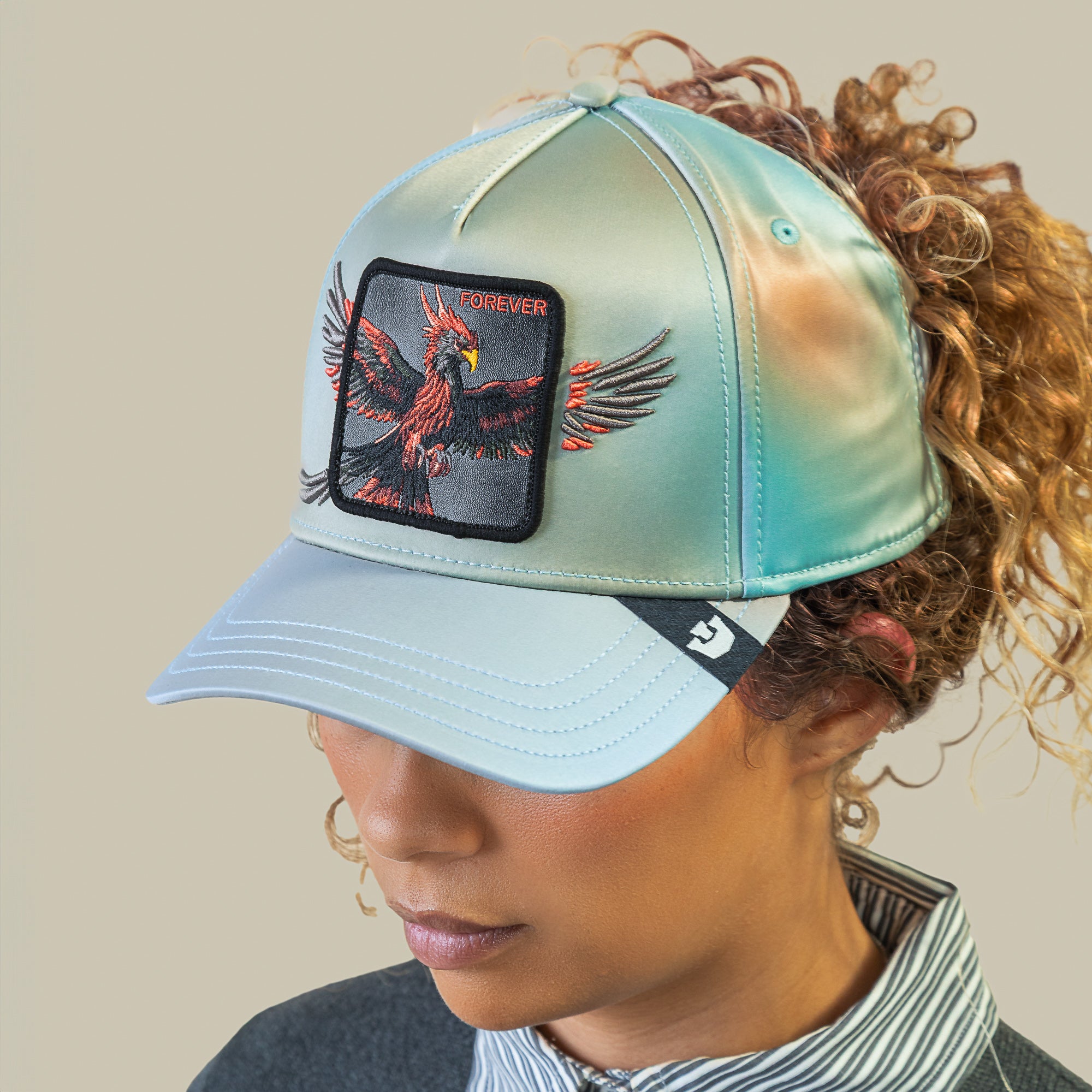A person wears Goorin Bros.'s "Never Stop Never Stopping" light blue cap featuring a sky-blue crown, an embroidered black and red bird patch, and FOREVER on the front—capturing that forever style.