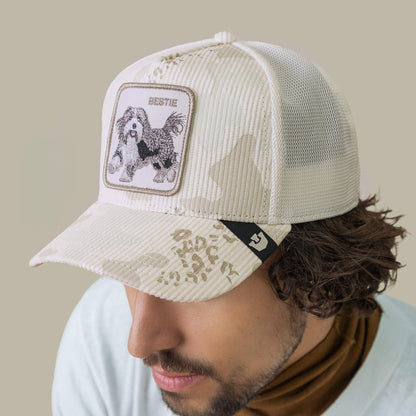 A man wears the Goorin Bros. Bestie Camo cap, featuring a shaggy pup patch and "BESTIE" on the front, plus an off-white snow camo brim for a playful, stylish look.
