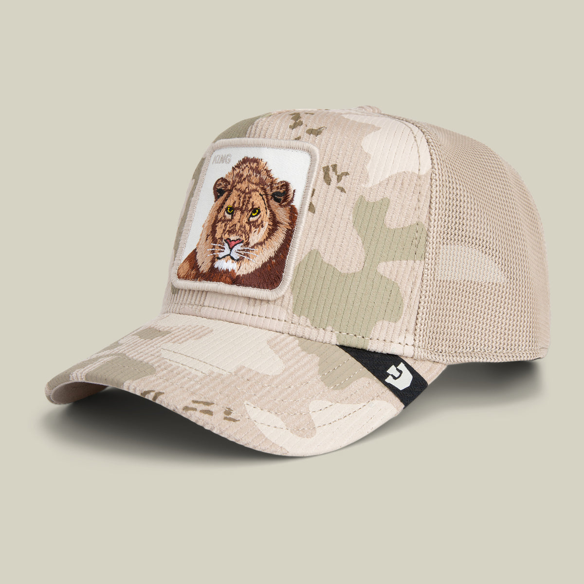 The King Camo hat by Goorin Bros. is a beige camouflage cap with a mesh back and a patch featuring a lion’s face on the front panel.