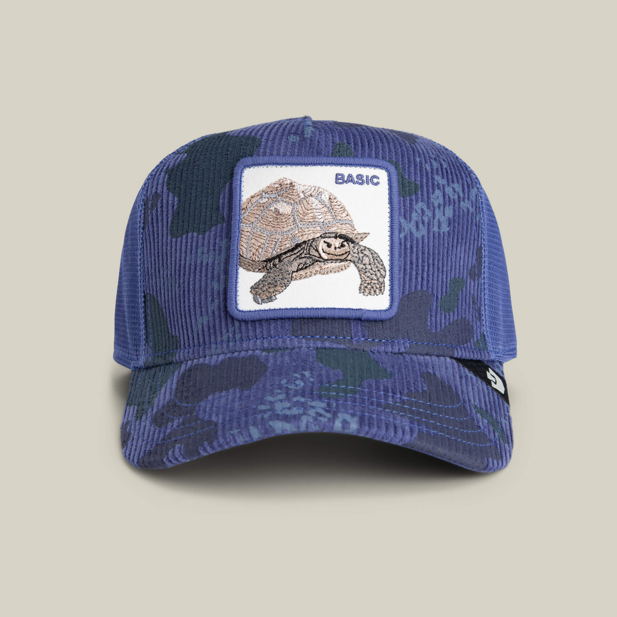 The Turtle Camo hat by Goorin Bros. features blue camo corduroy, a front patch with a tortoise and "BASIC," and a mesh back for ventilation, set against a plain beige background. Ideal for fans of the Turtle Camo style.