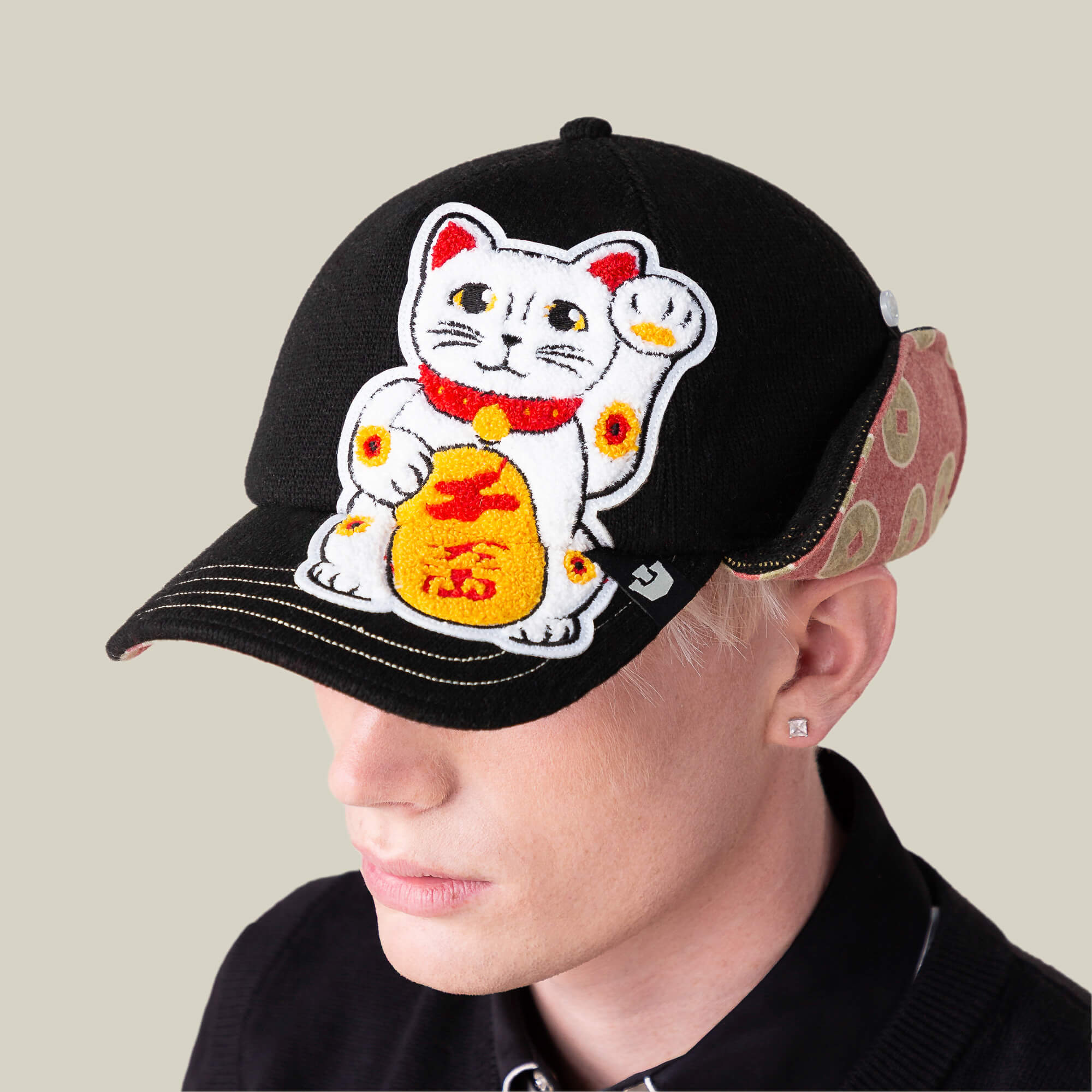 Person wearing the "F is for Fortune" black baseball cap by Goorin Bros., featuring a large embroidered lucky-cat (maneki-neko) design on the front and patterned side fabric, adding winter charm.