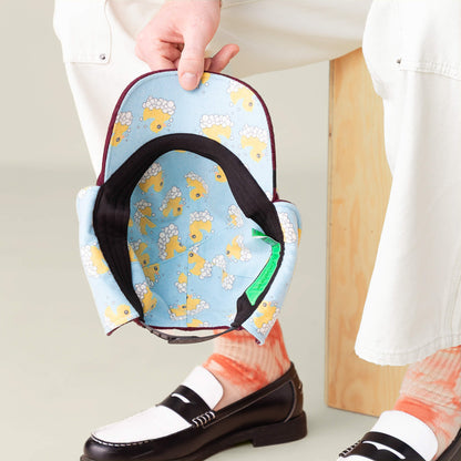 A person in white pants and loafers displays the inside of the Goorin Bros. "F is for Duck" light blue hat, featuring bubble print lining and a yellow duck design.