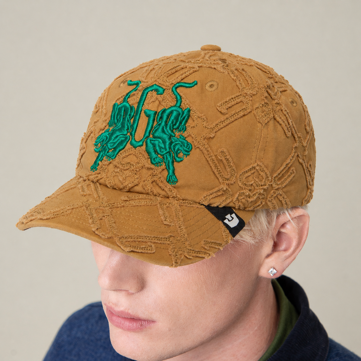 Wearing the Goorin Bros. "Future Baby Daddy" cap featuring green mirrored animals and a black tag, paired with a blue top and looking slightly down—serving main character energy.