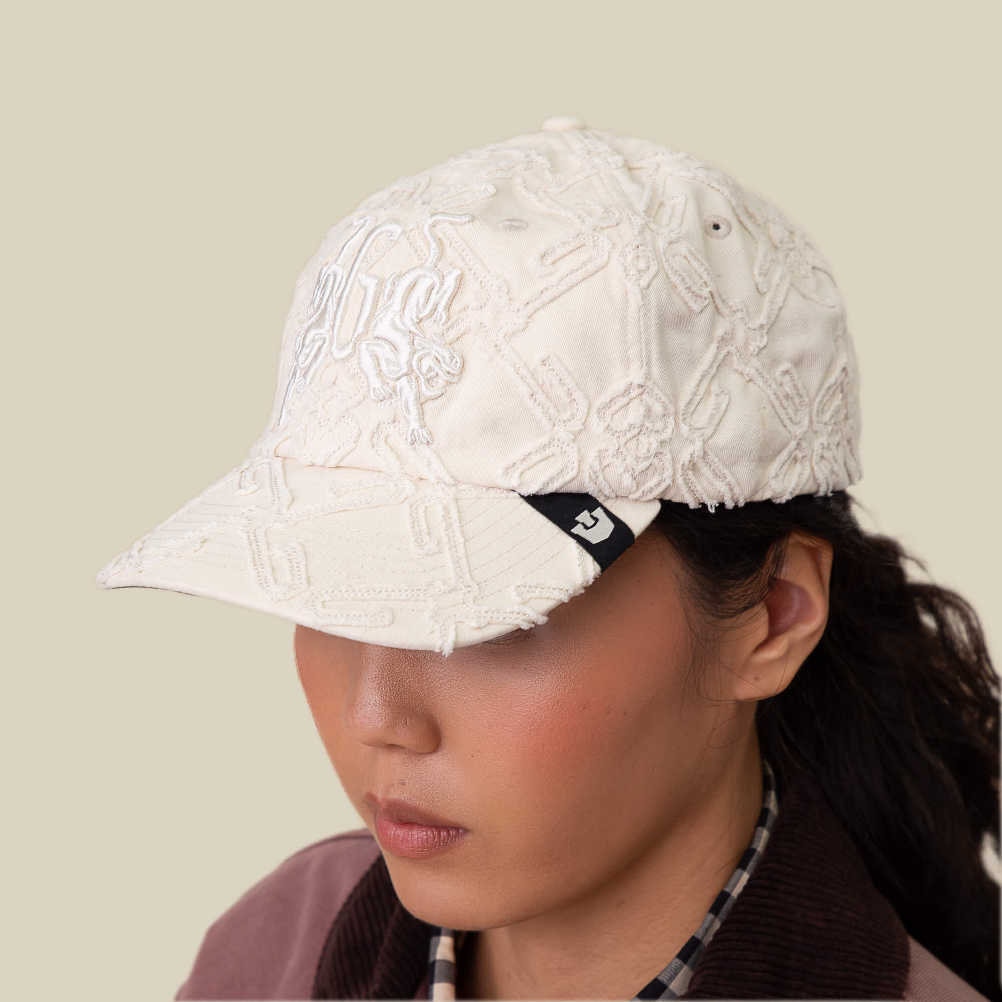 Person wearing the Goorin Bros. Future Baby Daddy cap in off-white with all-over embroidery, gazing downward against a plain beige background, exuding main character energy.