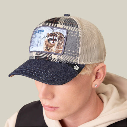 A person wearing the Goorin Bros. "Free Spirited" mesh baseball cap, featuring a plaid crown, denim brim, and raccoon patch, looks downward.