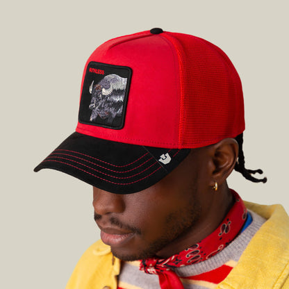 A person in the Goorin Bros. Suede Buffalo cap—red crown, black suede brim, buffalo patch—plus a red bandana, yellow shirt, and gold hoop earring, viewed slightly from the side against a plain background.