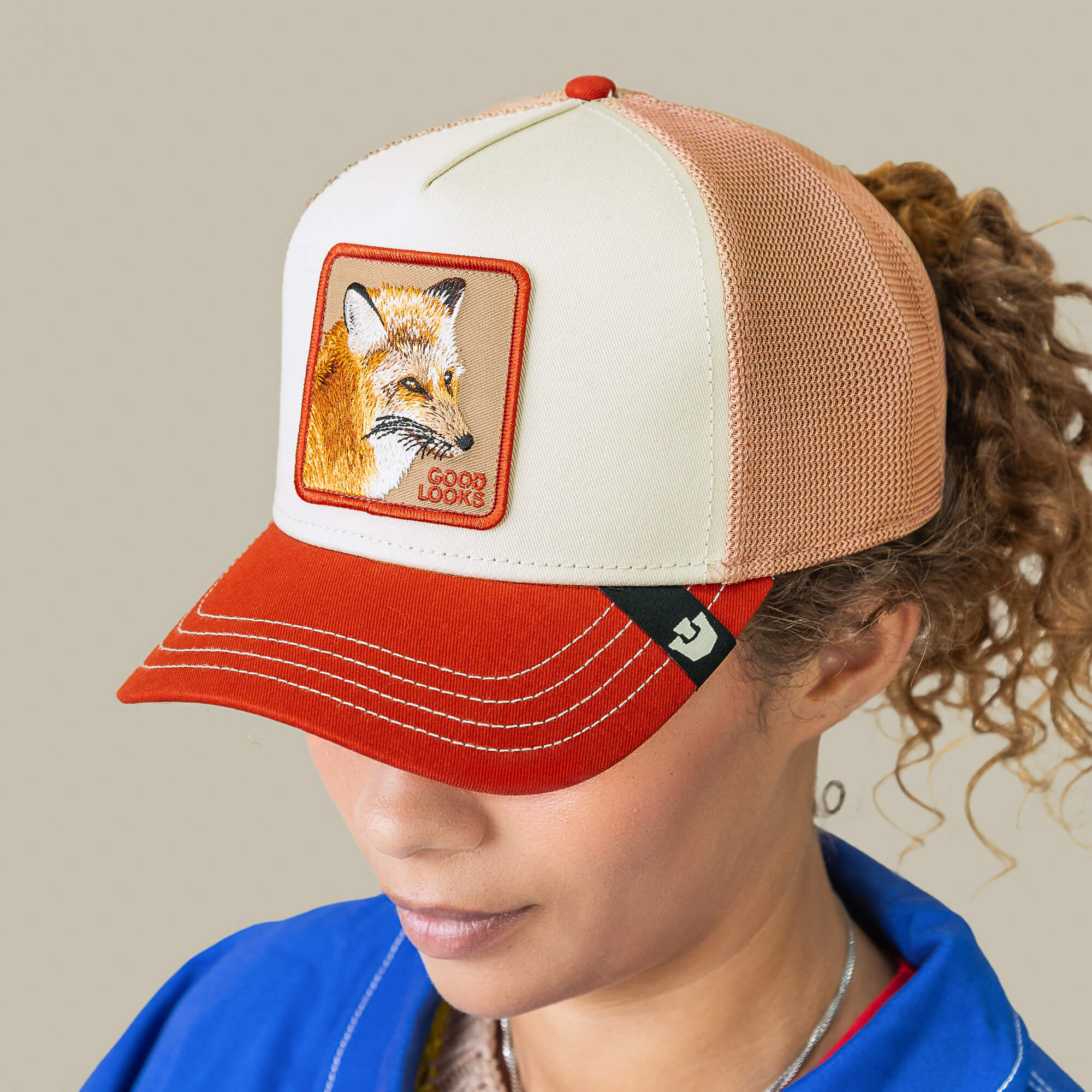 A person wears the Goorin Bros. Tricolor Fox trucker hat, featuring a fox patch labeled GOOD LOOKS, paired with a blue jacket against a plain background.