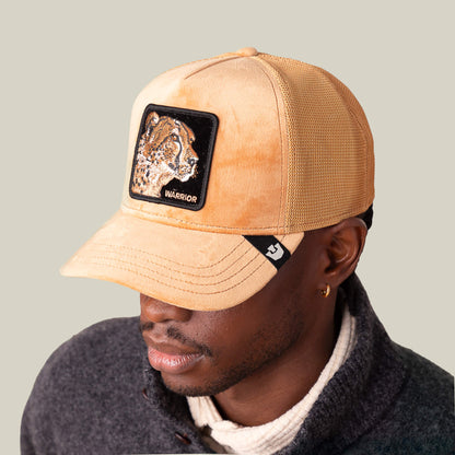A man sports the Goorin Bros. Velour Cheetah tan baseball cap, featuring a WARRIOR patch, paired with a dark jacket over a light turtleneck for a look that combines sleek motion with modern style.