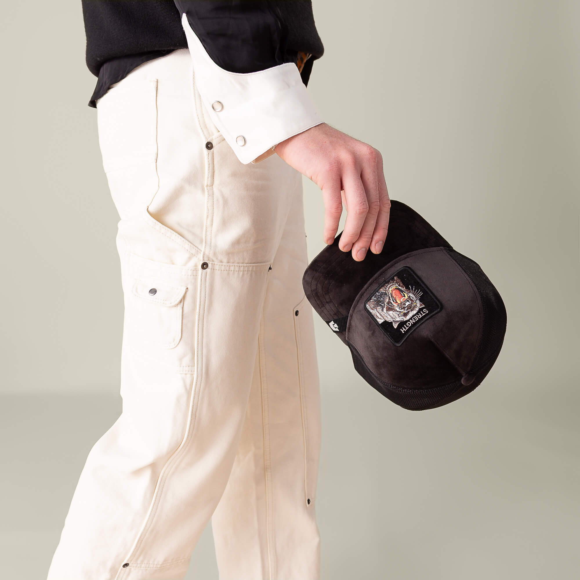 A person in off-white pants and a black-and-white shirt holds the Goorin Bros. Velour Panther hat in their right hand against a neutral background.