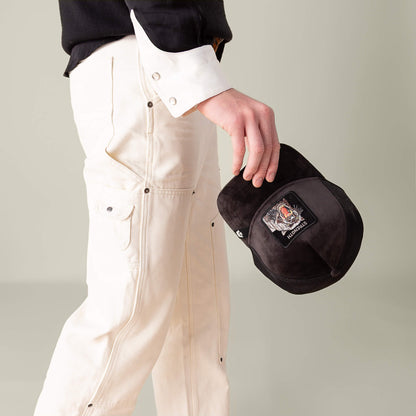 A person in off-white pants and a black-and-white shirt holds the Goorin Bros. Velour Panther hat in their right hand against a neutral background.