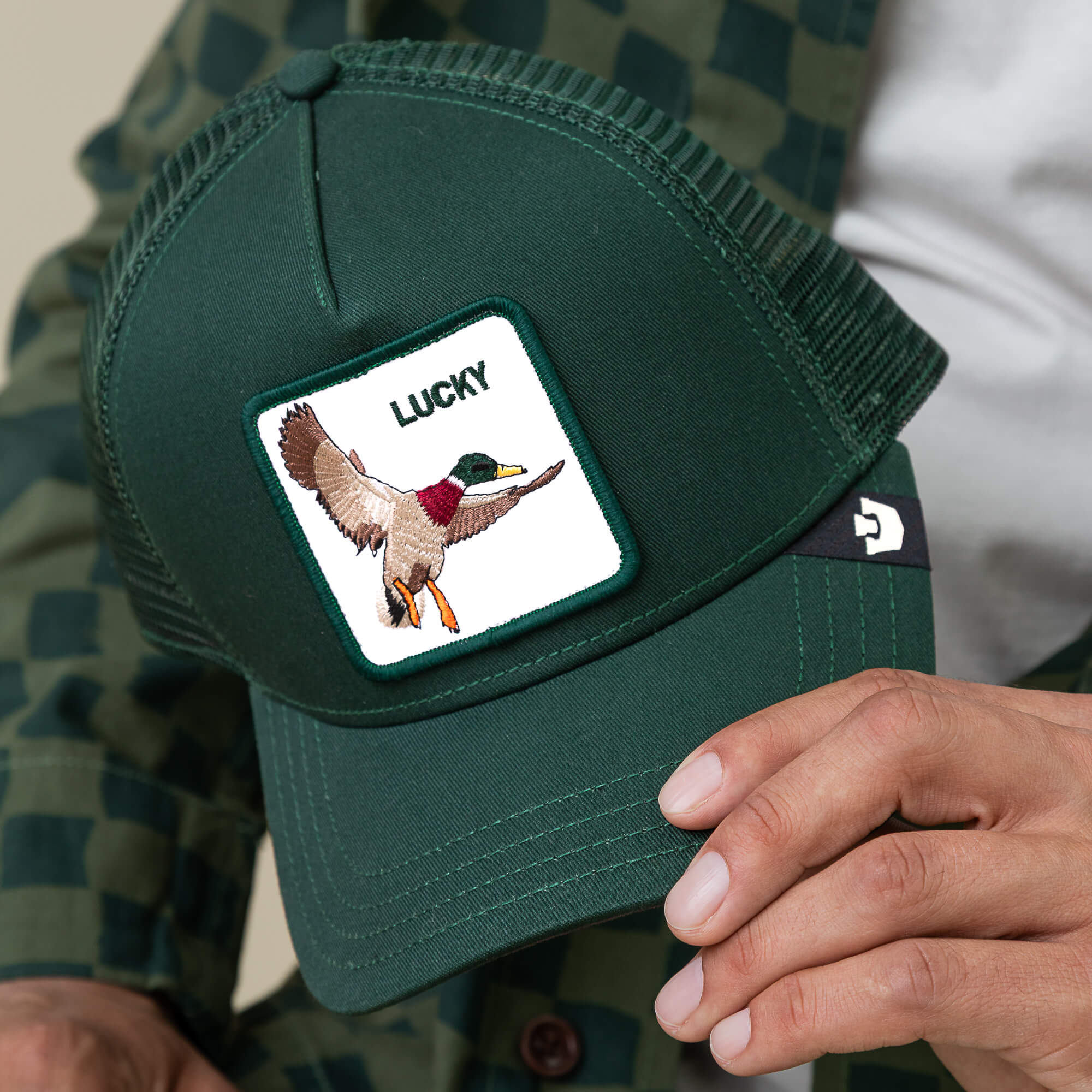 A person holds The Lucky Duck trucker hat by Goorin Bros., featuring a bird patch with a flying duck and "LUCKY" above it—a perfect good luck charm.