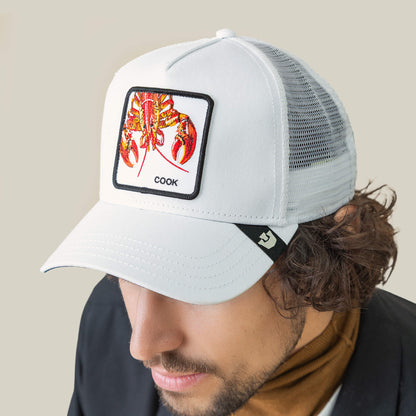 Someone wears the Goorin Bros. Lemme Cook white mesh back trucker hat, featuring a playful illustrated lobster patch and the word "COOK" on front.